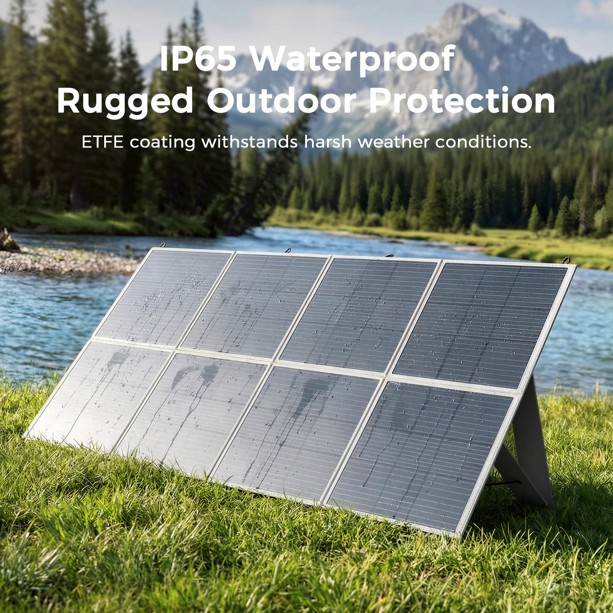 An eight-panel foldable solar panel is set up in a grassy field near a river, with mountains in the background.