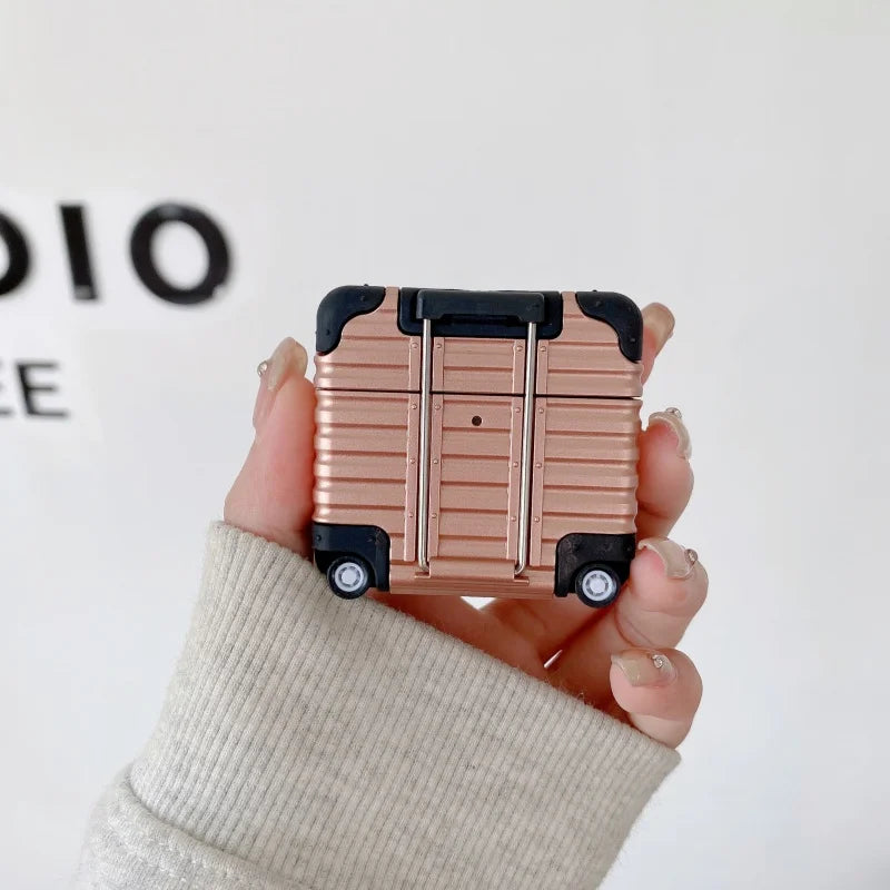 Rose gold suitcase-style hard shell AirPods case with black corner details, held in a hand.