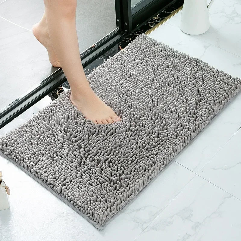 A grey, absorbent shaggy doormat with a soft, noodle-textured surface, shown on a tiled floor.