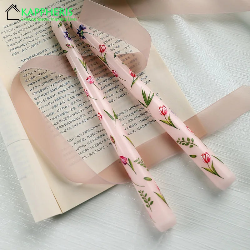 Two pale pink tapered dinner candles decorated with delicate red tulip and green leaf floral prints.