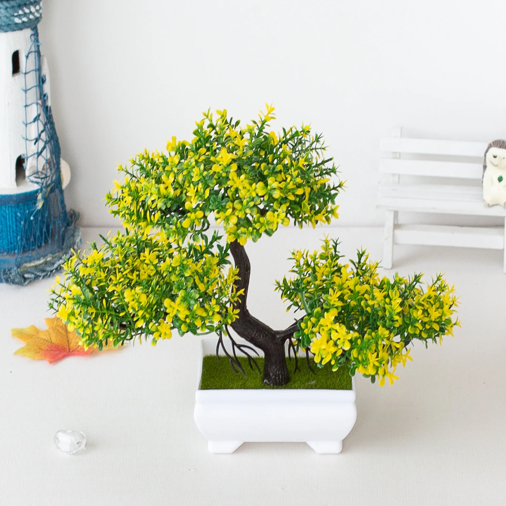 Artificial bonsai tree with vibrant yellow-green leaves in a small, square white pot, set against a light background.