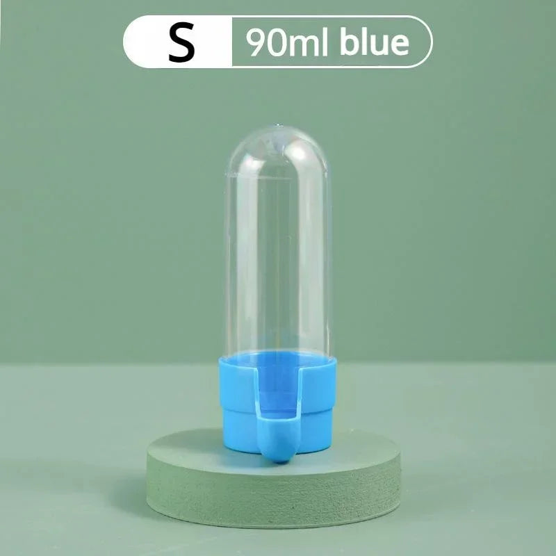 Small 90ml clear plastic bird water dispenser with a blue base, standing on a green circular pedestal.