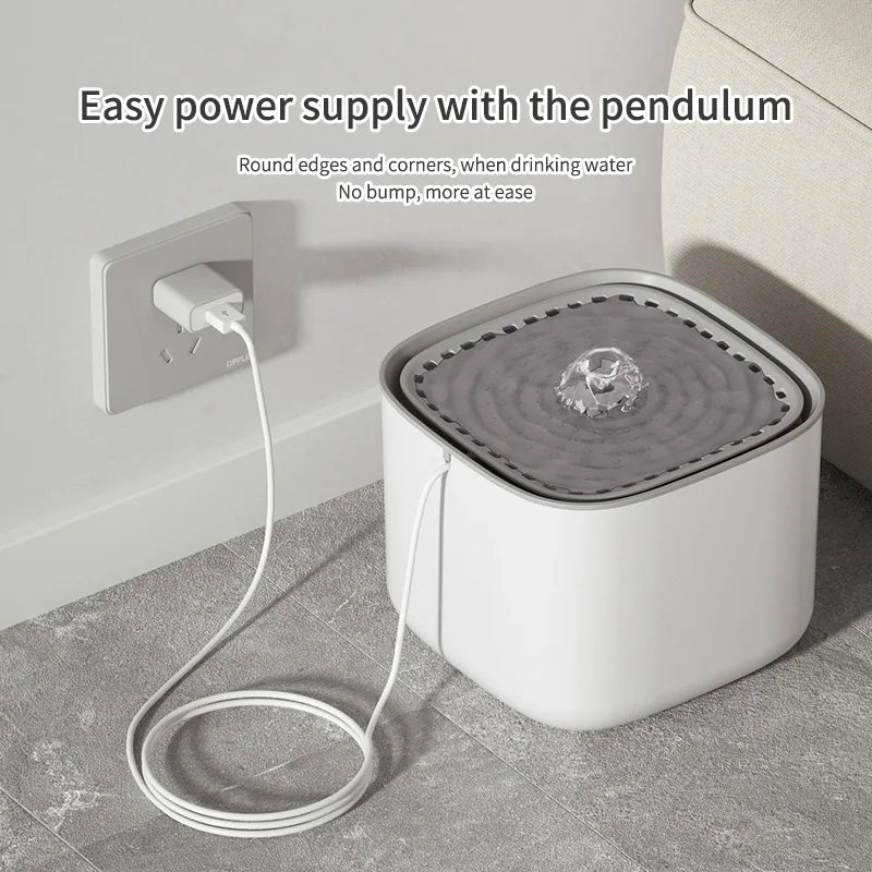 White square pet water fountain with a grey top basin, plugged into a wall outlet. Minimalist, modern design.