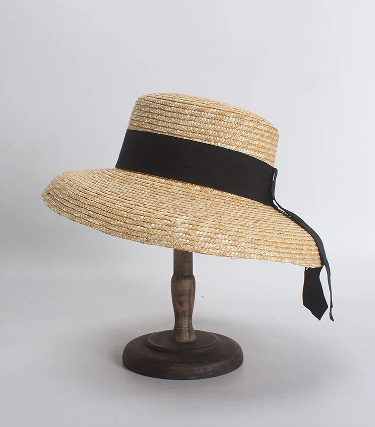 Elegant natural straw sun hat with a wide brim and a black ribbon tied in a bow at the side on a display stand.