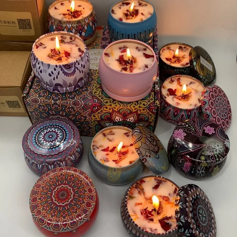 Collection of scented candles in patterned, colourful metal tins with dried flower petals, some burning with lit wicks.