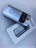 Silver wireless smart video doorbell with motion detection and camera lens, resting on its product packaging.