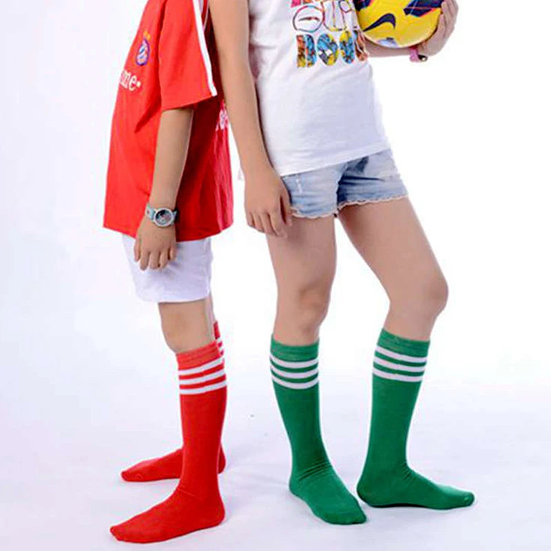 Children wearing mid-calf cotton socks in bright red and green, featuring classic white triple-stripe athletic detailing.