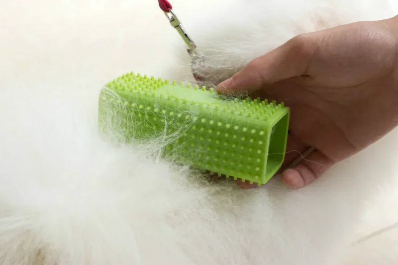 A hand holding a lime green, rectangular silicone pet hair remover brush against white fur.