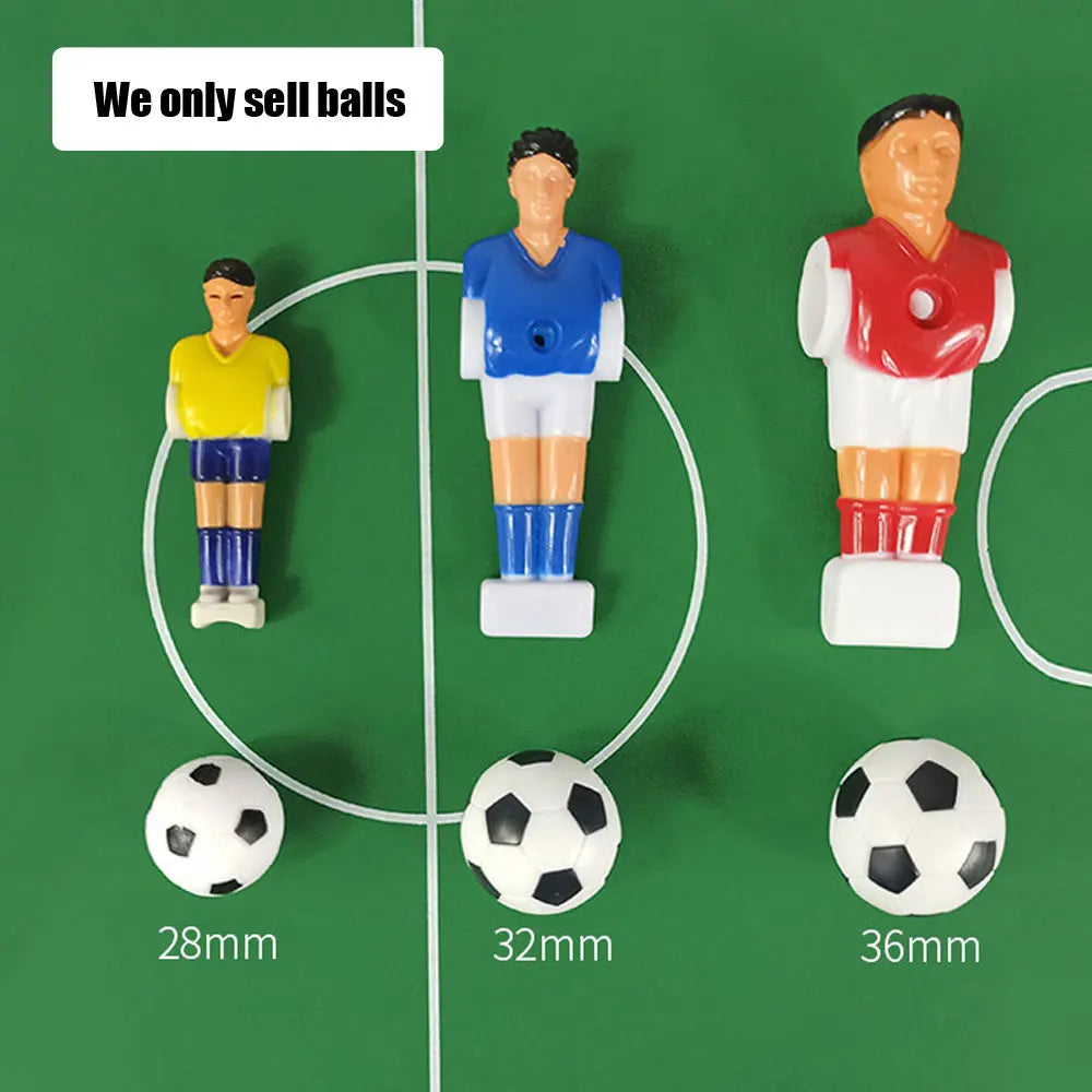 Three black and white plastic table football balls in 28mm, 32mm, and 36mm sizes, shown on a green pitch.