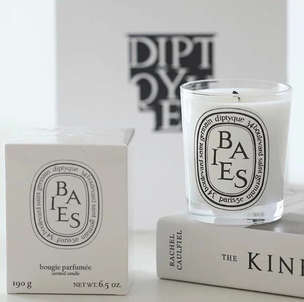 A white scented candle in a glass jar with a black and white oval label, displayed next to its matching gift box.