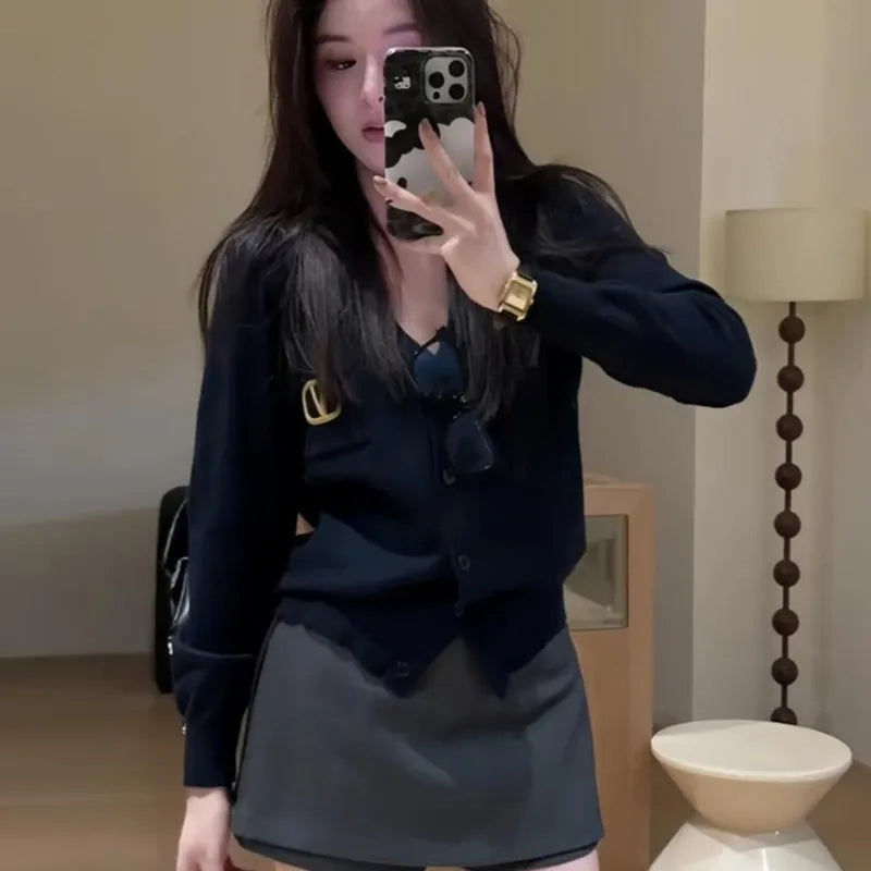 A woman wearing a black V-neck button-down cardigan with a small gold embellishment and a plain grey mini skirt.