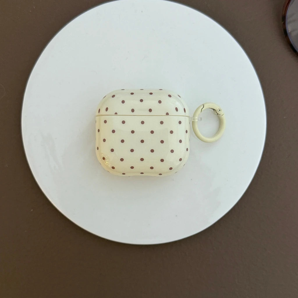 Cream AirPods case with brown polka dots, glossy finish, and circular attachment ring. Compatible with AirPods.