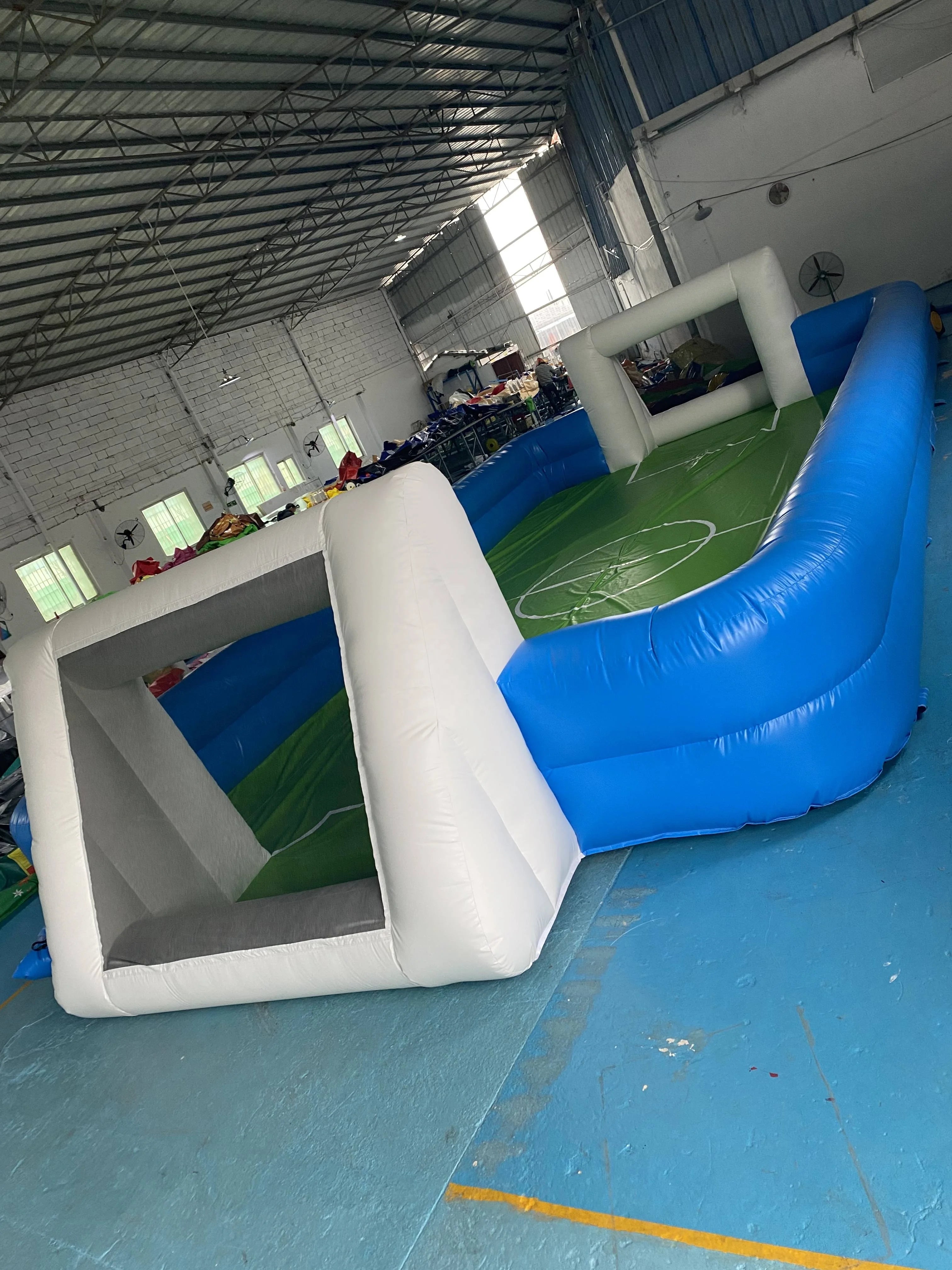 Inflatable football pitch with blue walls and white goalposts, featuring a green pitch marking.