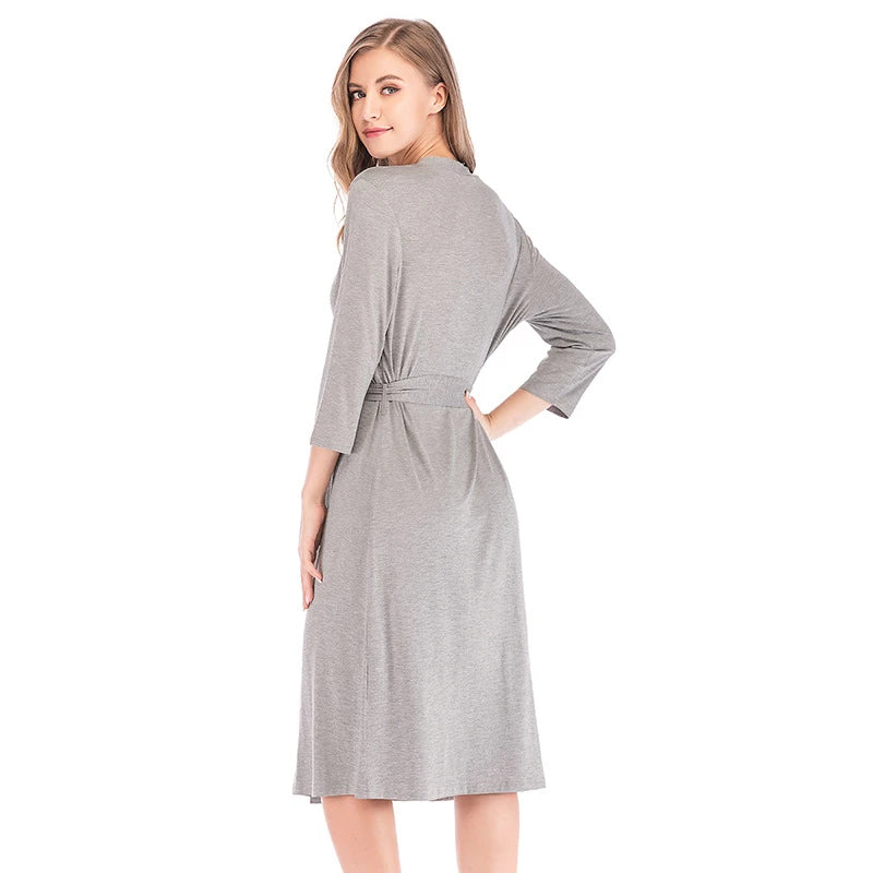 A woman wearing a knee-length, grey jersey dressing gown with three-quarter sleeves and a tie-waist belt.