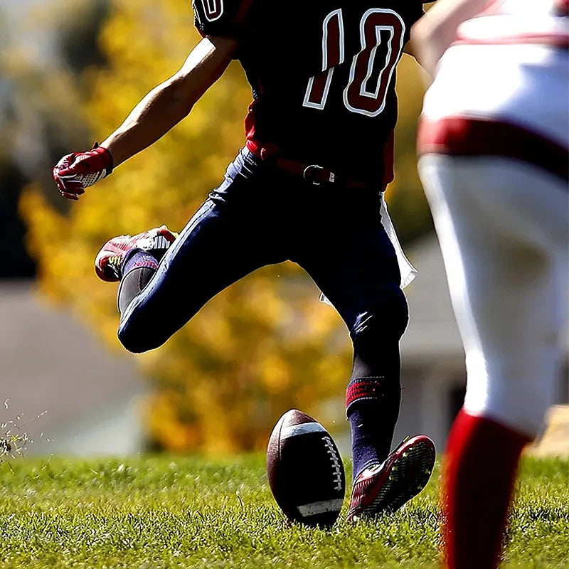 American football player in a black and red uniform kicking a ball on a grass field.