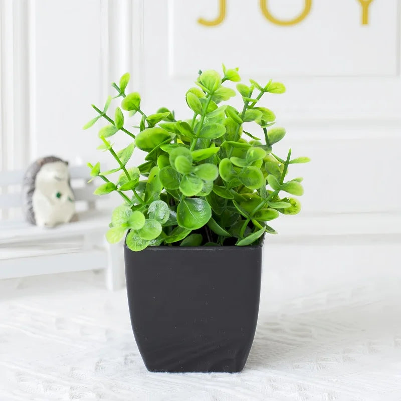 A small, vibrant green artificial plant with rounded leaves potted in a simple, matte black square container.