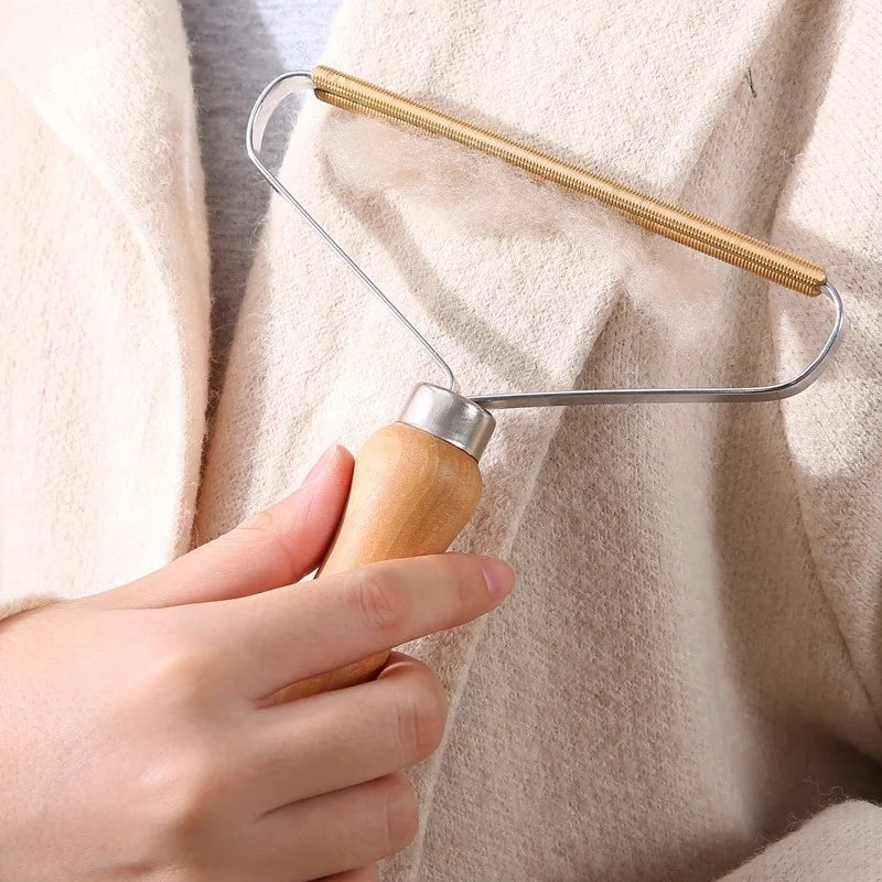 Hand using a portable lint remover with a wooden handle and copper head on a cream wool coat.