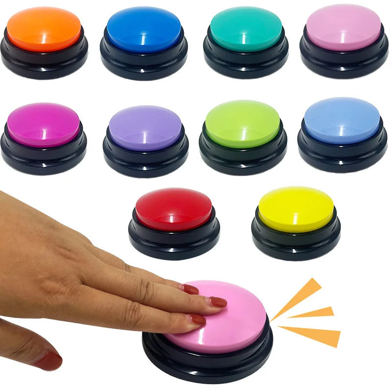 A hand presses a pink recordable dog training button, surrounded by various colourful buttons in a circular black base.