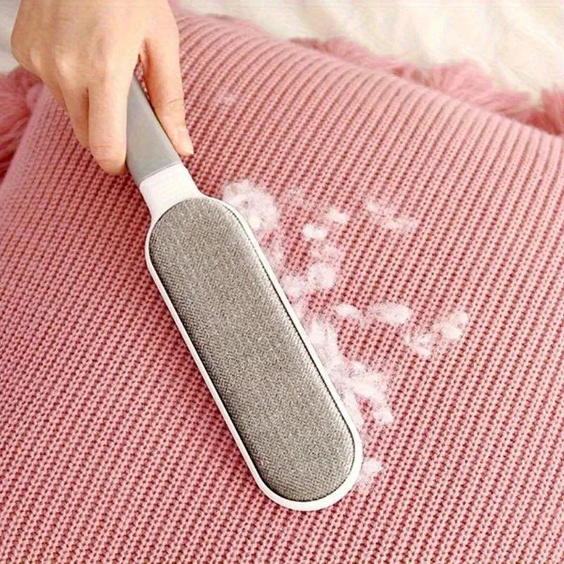 A white and grey lint remover brush cleaning white fluff off a textured, dusty pink knitted cushion.