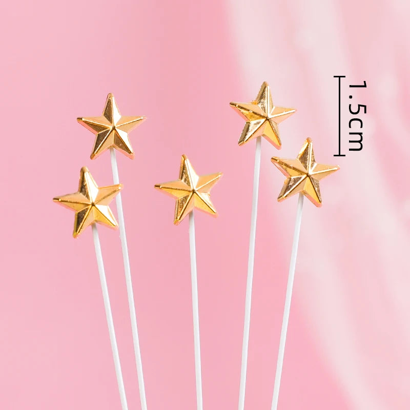 Five gold star cake toppers on thin white sticks, each star measuring 1.5cm, set against a soft pink background.