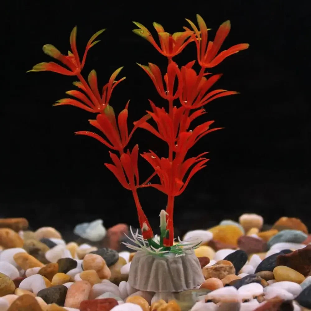 Artificial red aquatic plant with yellow-tipped leaves, anchored in a small base on a bed of multi-colored aquarium gravel.
