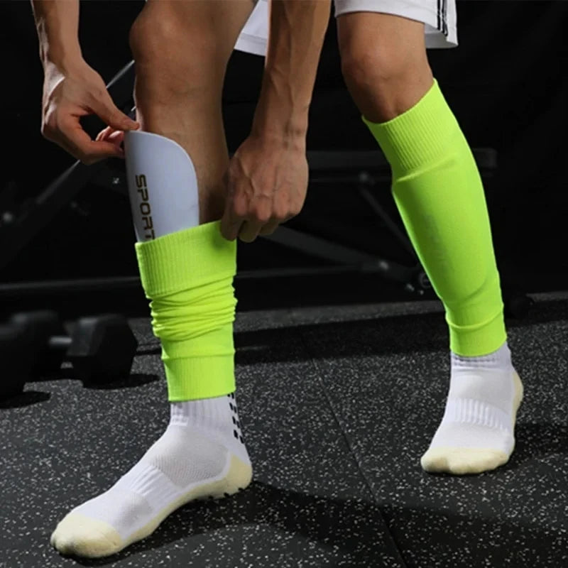 Neon green football shin guard sleeves being worn with white sports socks in a gym setting.