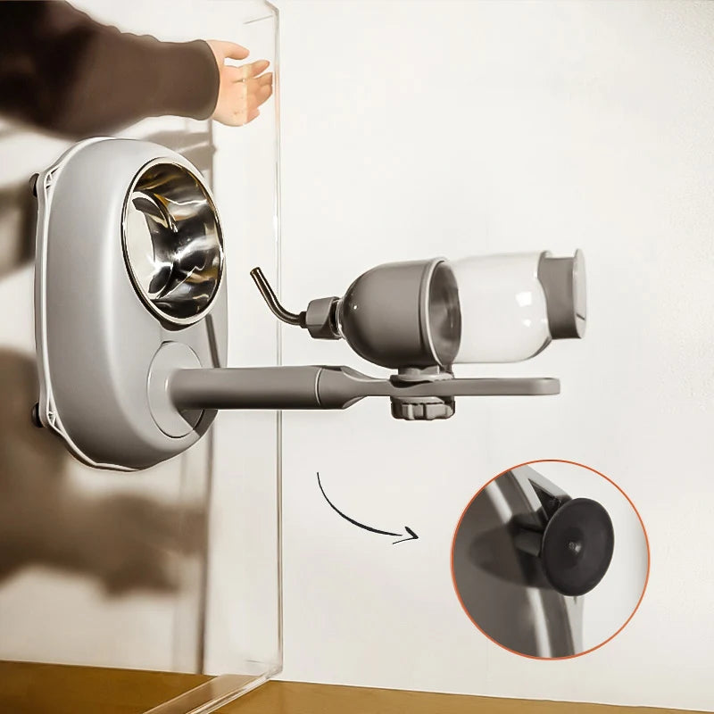 Grey pet feeder with metal bowl and attached clear water bottle mounted on wall via suction cups.