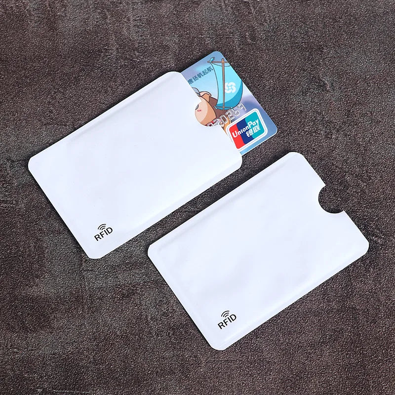 Two white plastic RFID-blocking sleeves for credit cards, with thumb cutouts, on a textured grey background.