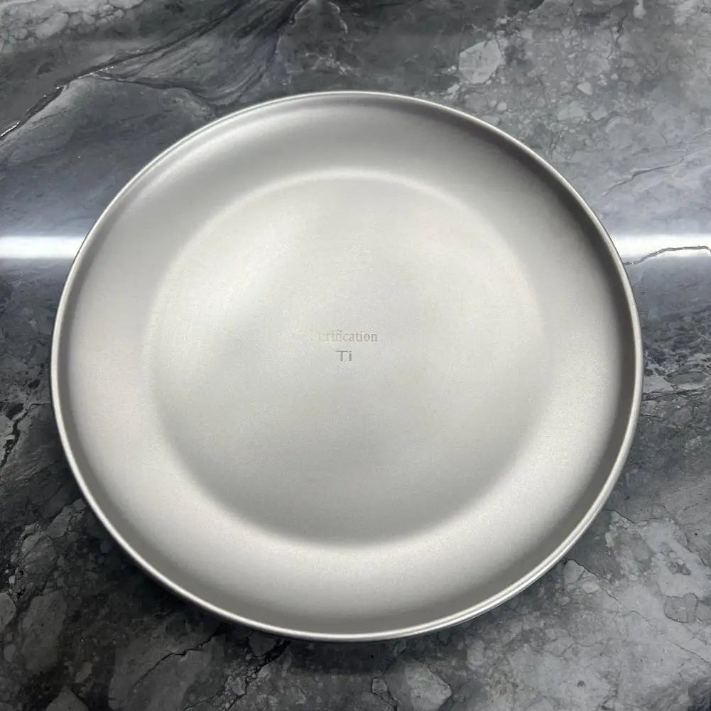 A round, matte gray titanium plate on a dark marble surface.