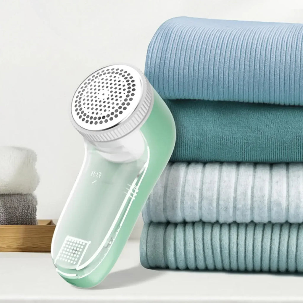 A mint green fabric shaver with a metal mesh head, placed next to a stack of folded blue ribbed textiles.