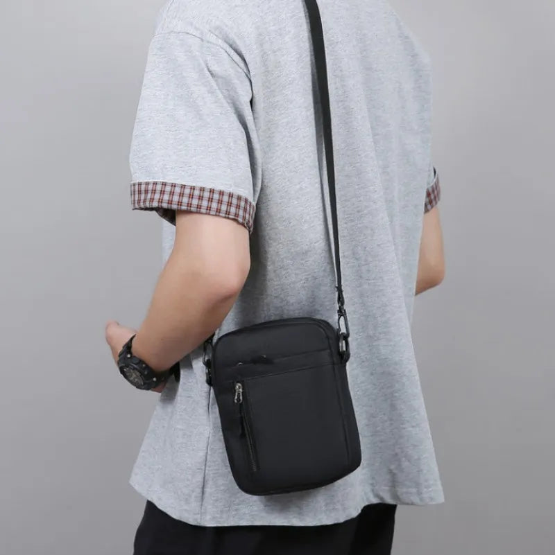 A man wearing a practical, black rectangular crossbody bag with an adjustable strap and front zip pocket.