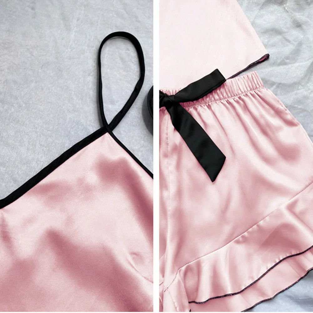 Pink satin pyjama set featuring a camisole with black straps and matching frill-hem shorts with a black bow tie.
