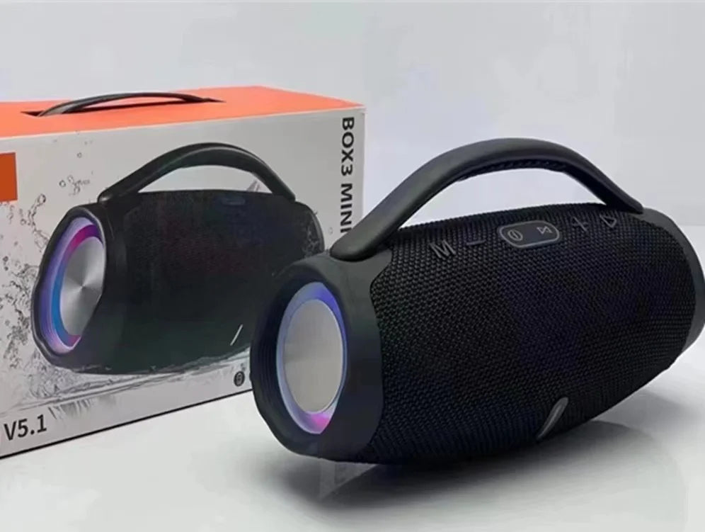 Black portable Bluetooth speaker with a carry handle, side RGB lighting rings, and fabric mesh finish, shown with its box.