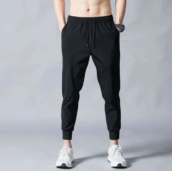 Men wearing black, slim-fit joggers with an elasticated drawstring waistband and cuffed ankles against a grey background.