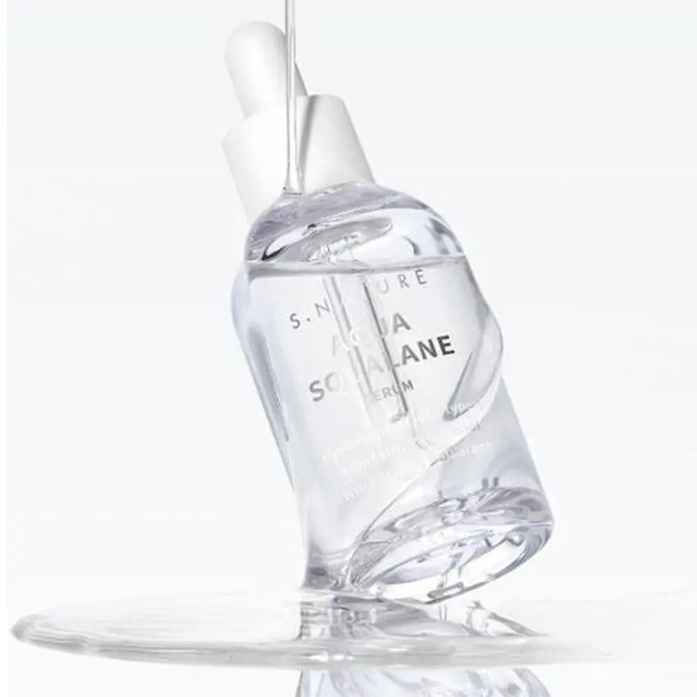 Clear facial serum bottle with dropper top, shown tilted with liquid pouring over it onto a reflective surface.