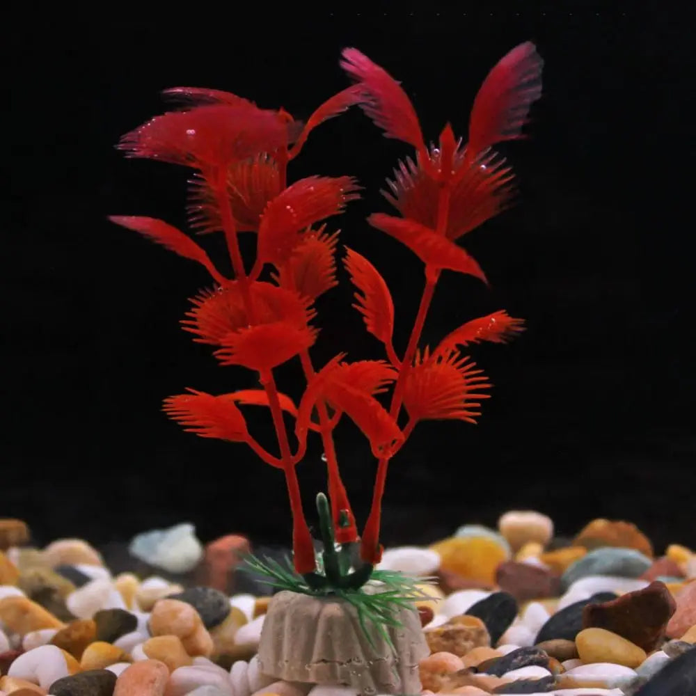 Artificial red aquarium plant with feathery leaves, set in a weighted base on a bed of multi-colored gravel.