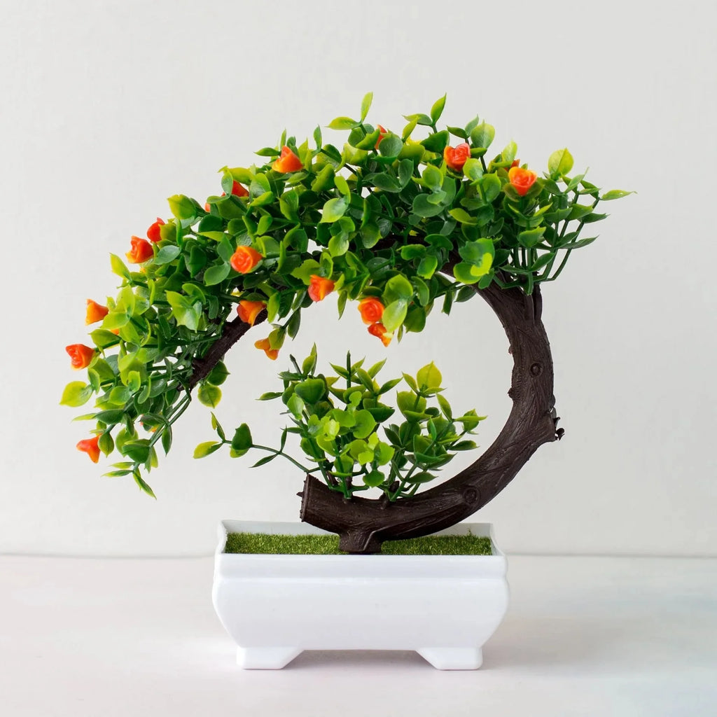 Artificial bonsai tree with green leaves and small orange flowers in a white rectangular pot on a white background.