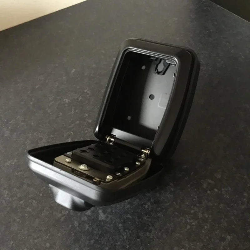 Open black metal key safe box with a push-button combination lock mechanism on a dark surface.