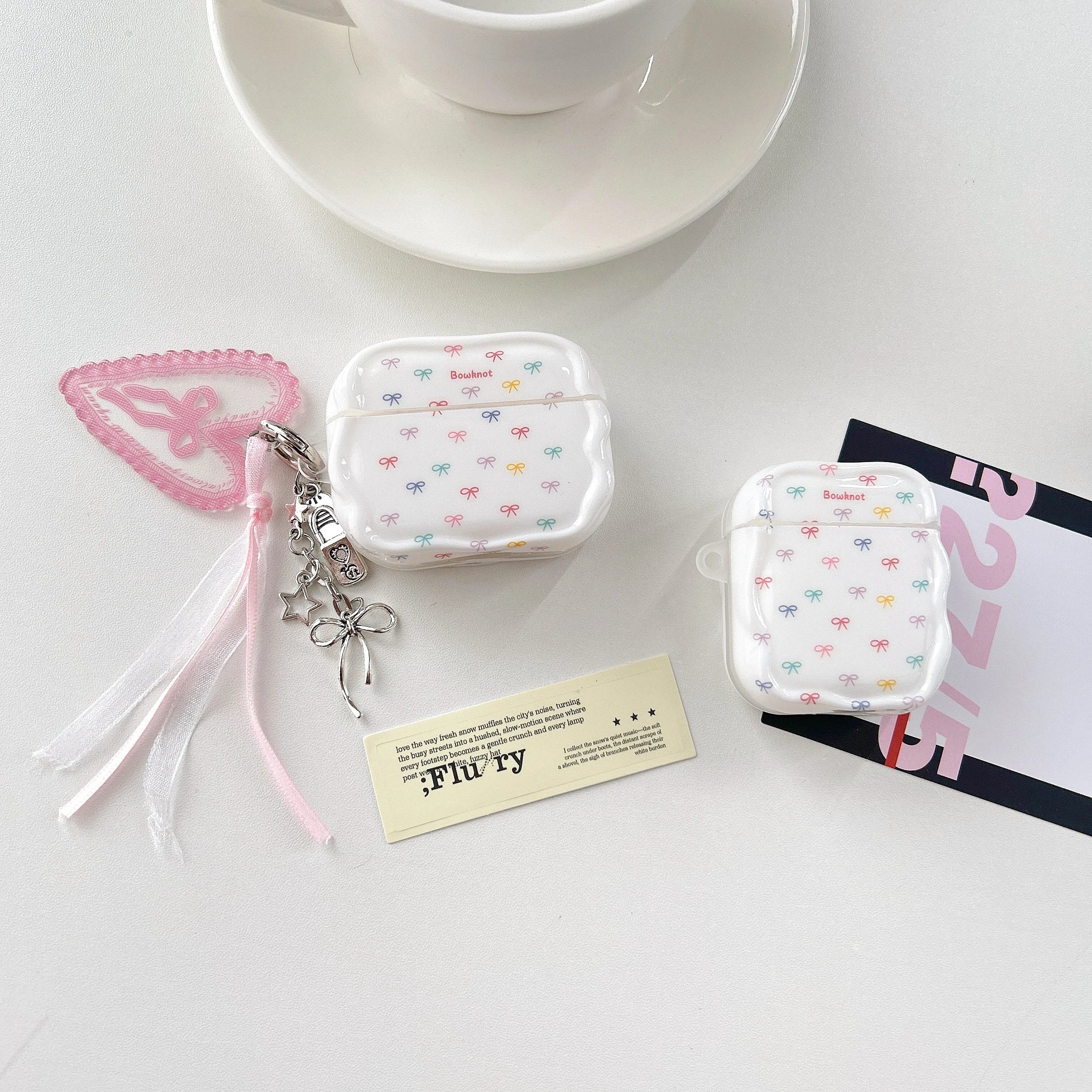 White glossy AirPods case with multi-coloured bow print and ribbon charm. Fits AirPods 1/2 and Pro models.