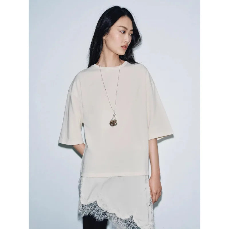 Model wearing a cream, oversized t-shirt with a layered, asymmetrical hem featuring delicate lace trim.