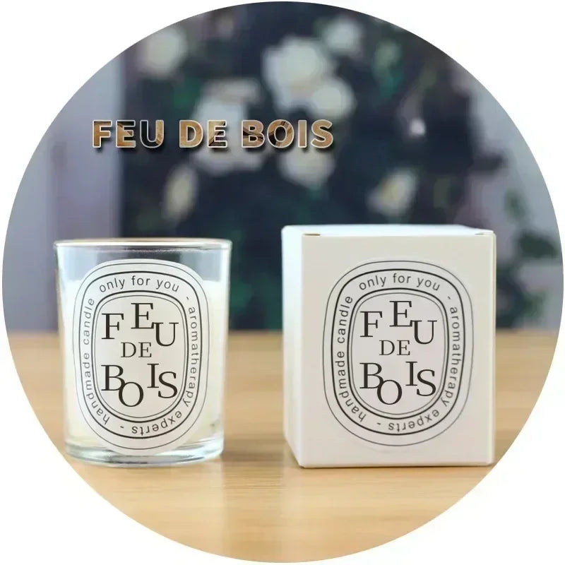Clear glass scented candle and white box with elegant black oval "Feu de Bois" aromatherapy label on wooden surface.
