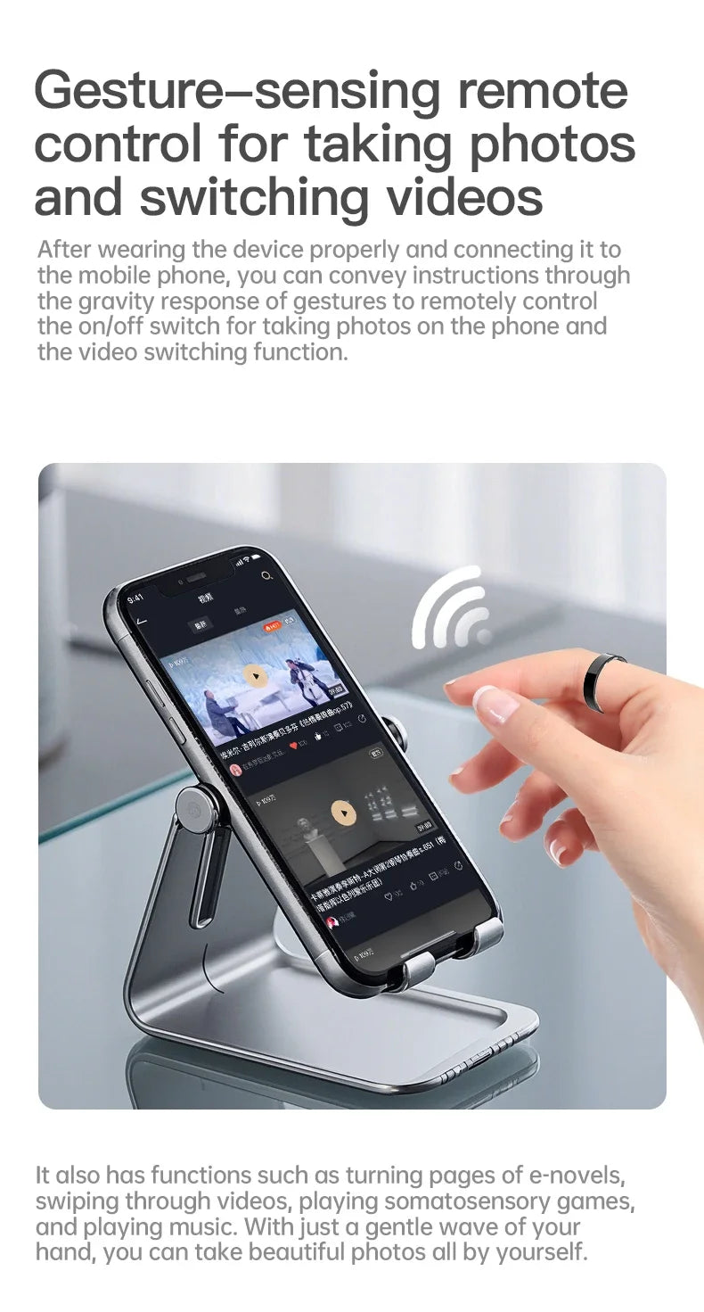 A sleek black smart fitness ring worn on a finger, used to remotely control a smartphone on a stand via hand gestures.