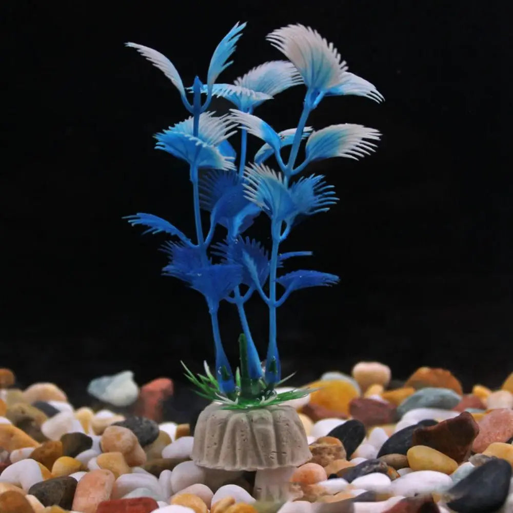 Artificial aquarium plant with blue, feathery leaves and white tips, set in a weighted stone base on colored gravel.