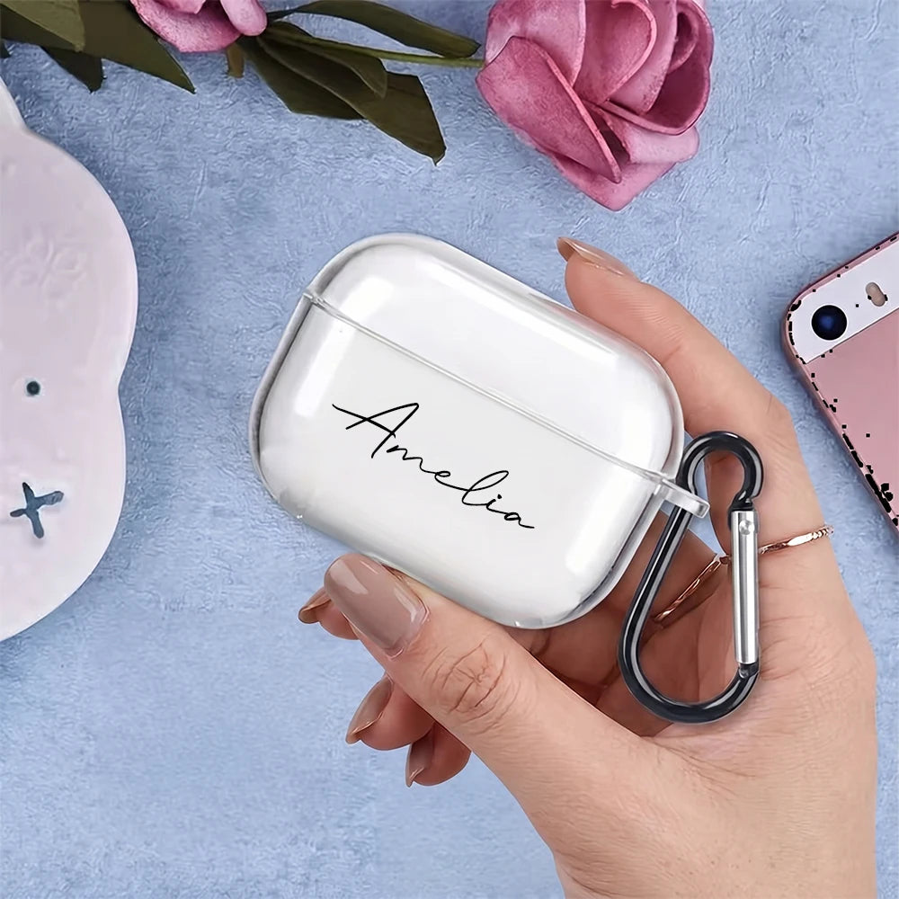 Clear personalised AirPods Pro case with 'Amelia' script text and a black carabiner clip, held in a hand.