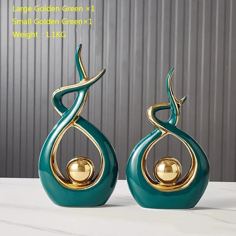 Two abstract ceramic ornaments in glossy emerald green and gold, featuring a central sphere and elegant curved design.