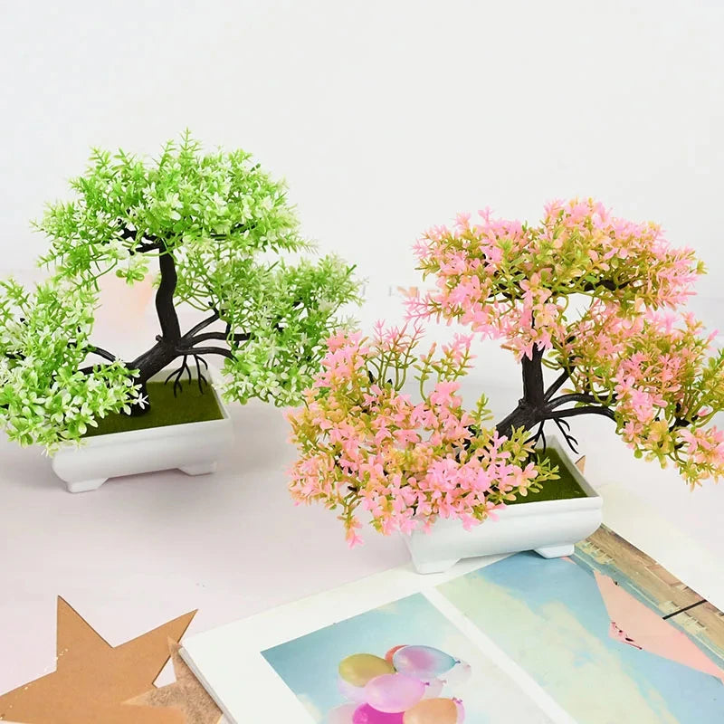Two artificial bonsai trees in white rectangular pots, one with green leaves and one with pink leaves, on a table.