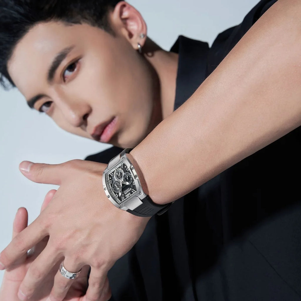 Man wearing a Mark Fairwhale wristwatch with a silver tonneau case, black dial, and black rubber strap.