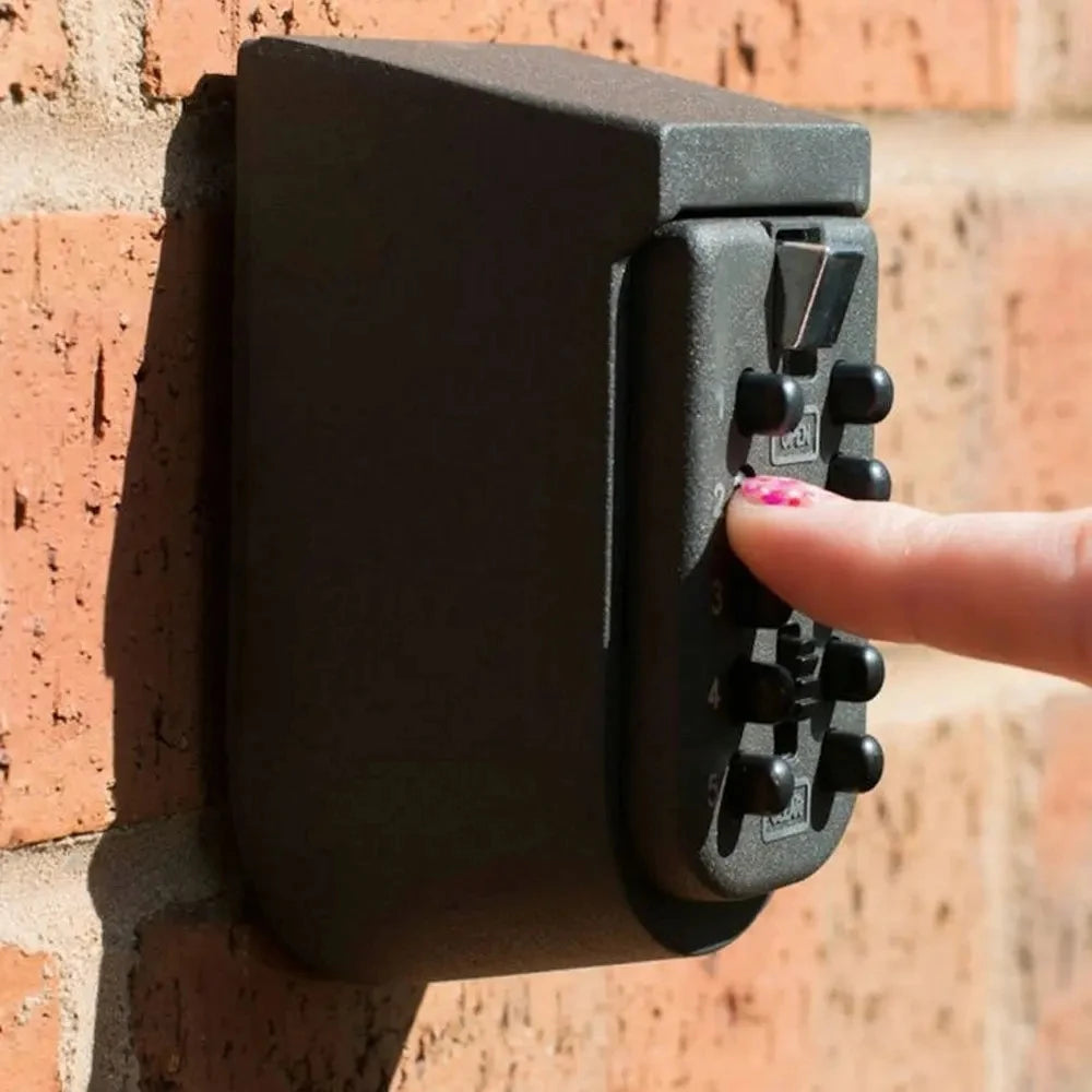 Dark gray wall-mounted key lock box with push-button combination entry, mounted on a red brick wall.