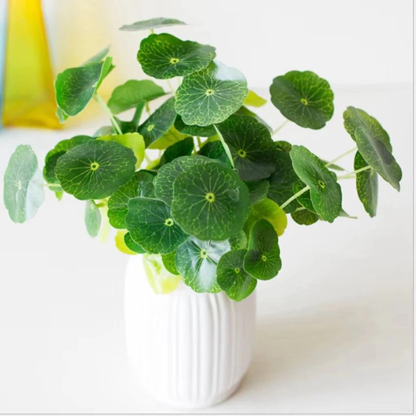 Artificial lotus plant with round, veined green leaves in a small, ribbed white pot against a bright background.