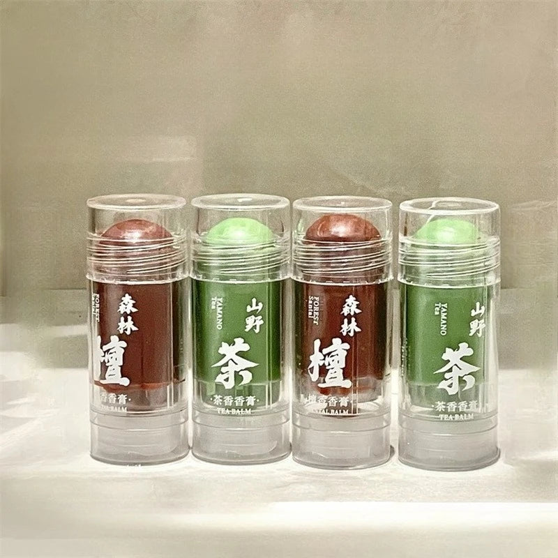Four cylindrical solid balm tubes in brown and green with clear caps and white text on the front.